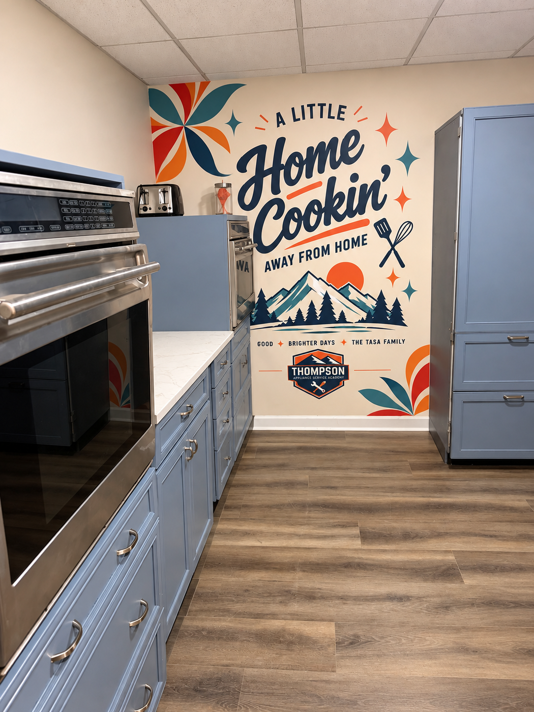 TASA Academy Kitchen with appliance range, blue cabinetry, and Home Cookin’ mural